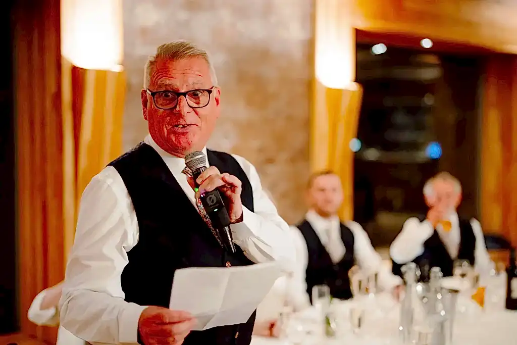 ARM1223-LOWRES-0800 a man holding a microphone and holding a paper as he delivers his speech via wedding live stream at elmore court wedding venue