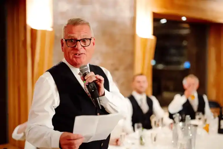 a man holding a microphone and holding a paper as he delivers his speech via wedding live stream at elmore court wedding venue