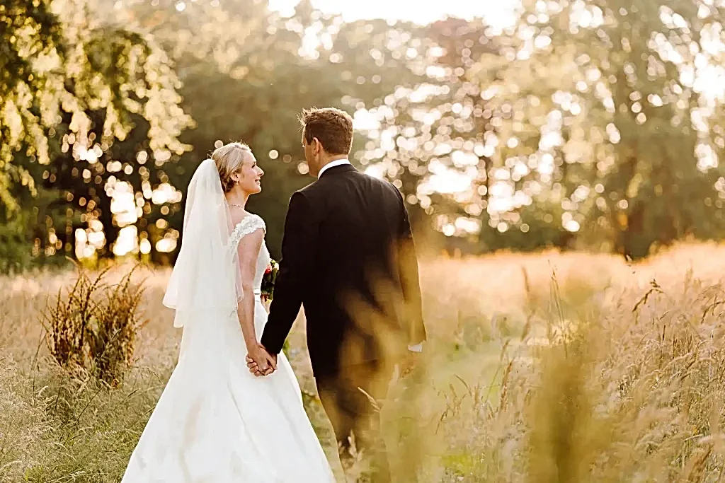 a groom and bride holding hands in a field in france as they pose for their wedding photographer