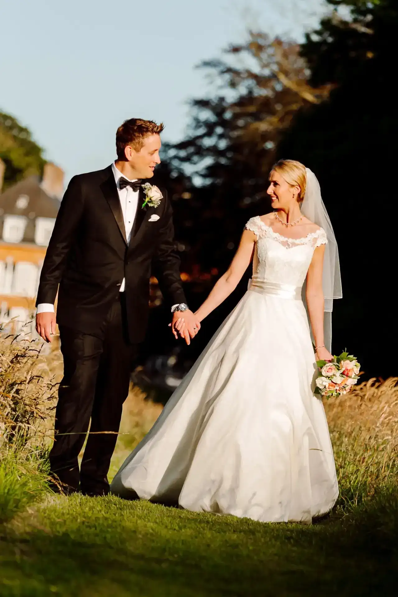 a bride and groom holding hands and walking in a field in france as they pose for their wedding photographer on their wedding day