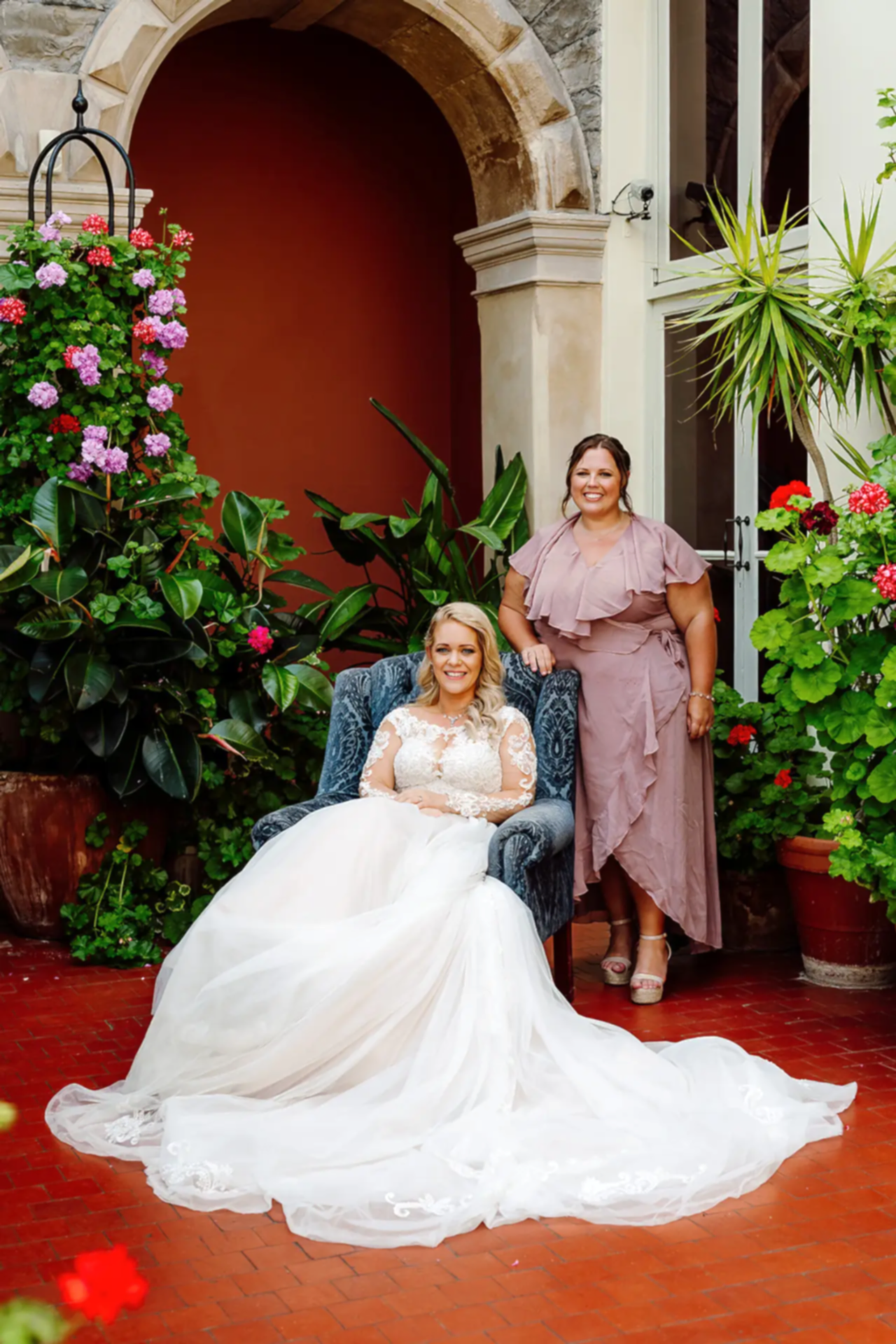 bride is sat down in chair in orangery of clevedon hall with her bridesmaid posing behind the chair
