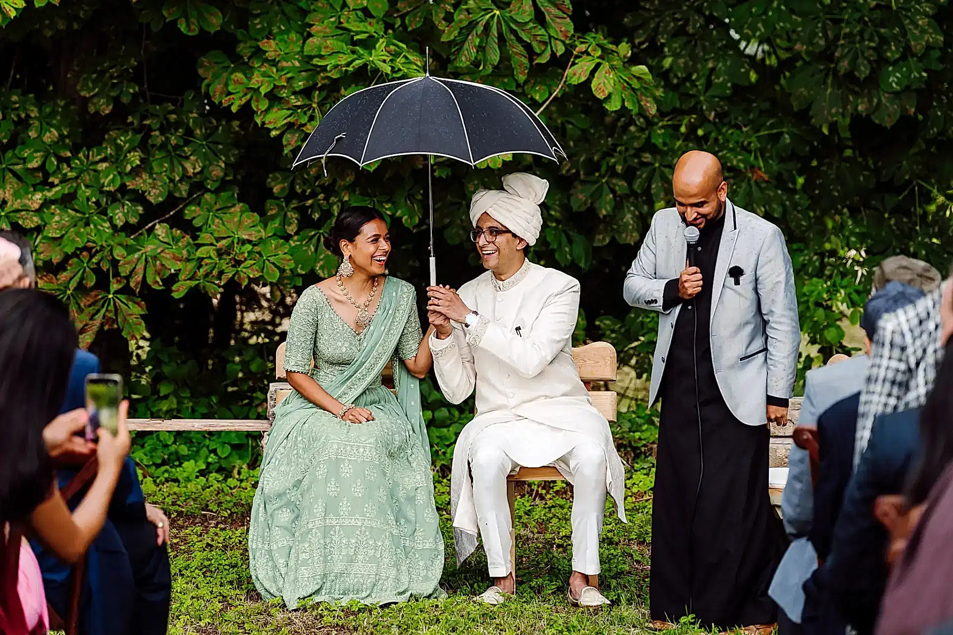 groom holds umbrella over his bride during their outdoor wedding ceremony on a rainy wedding day