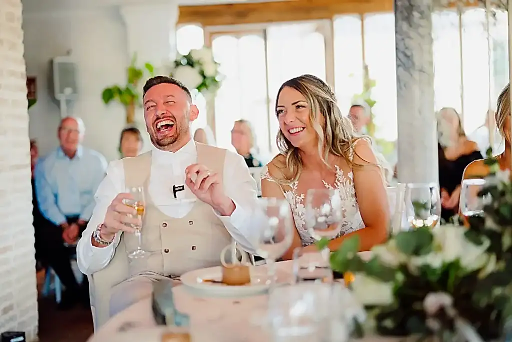 bride-groom-laughing-speeches-spain bride and groom laugh out loud while sat down listening to speeches at a wedding in finca monasterio in spain