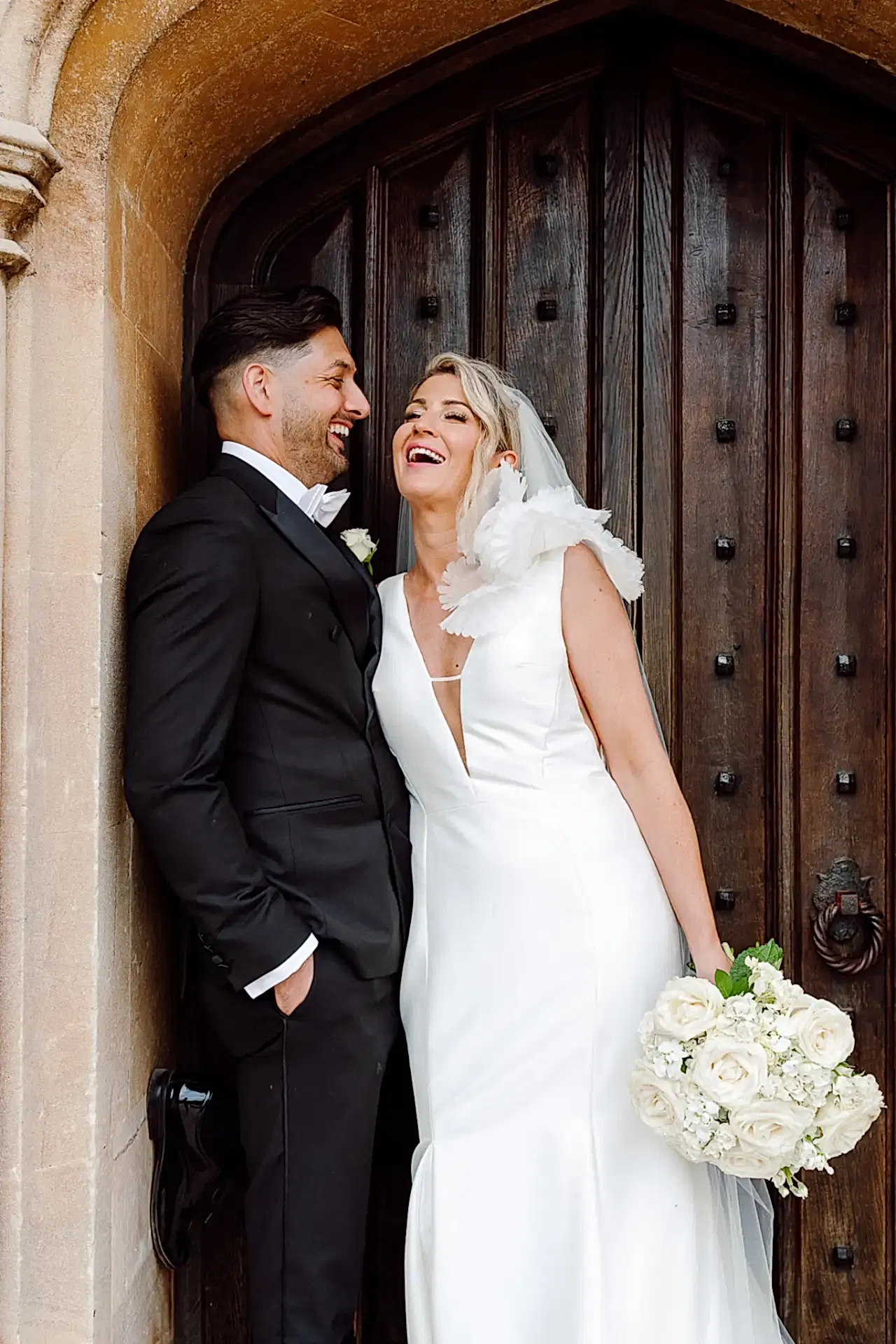 bride and groom lean against old stone doorway at st audries park and laugh in this candid wedding photo