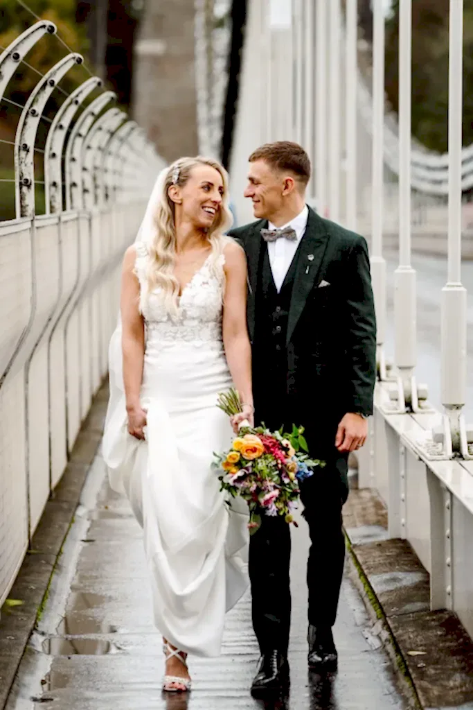 bride and groom walk down the middle of the clifton suspension bridge looking at one another in this example of bristol wedding videography