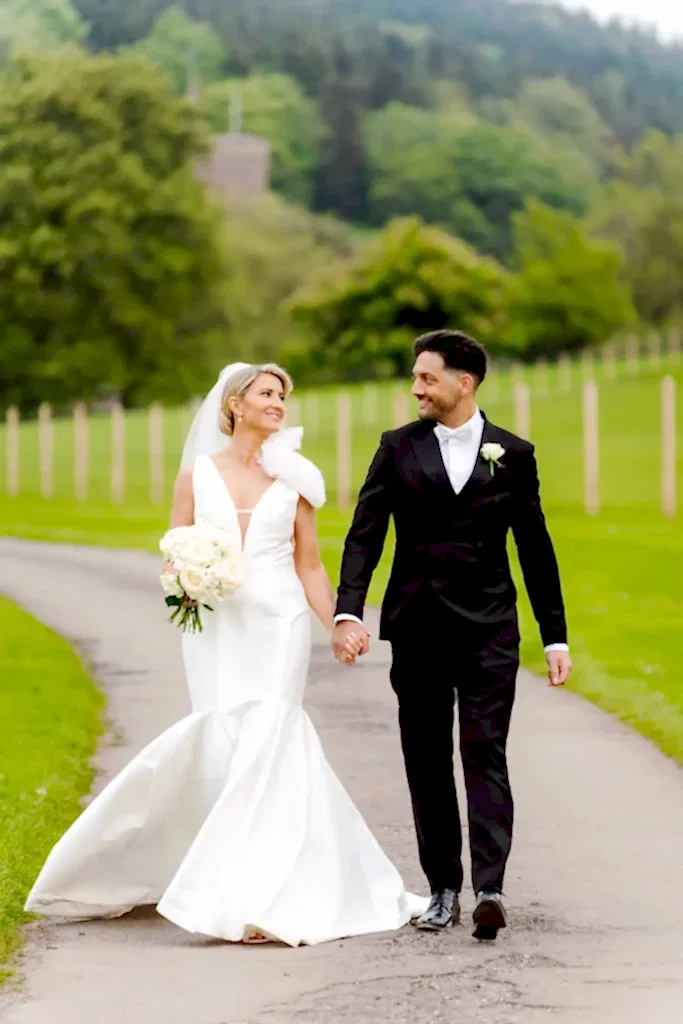 bride in white dress and groom in black suit and white bow tie are captured in this example of wedding videography as they walk hand in hand at St Audries Park in Somerset