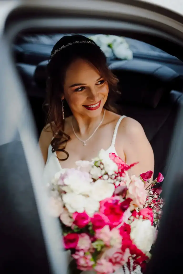 a somerset bride looks out of the wedding car holding her bouquet of flowers while smiling