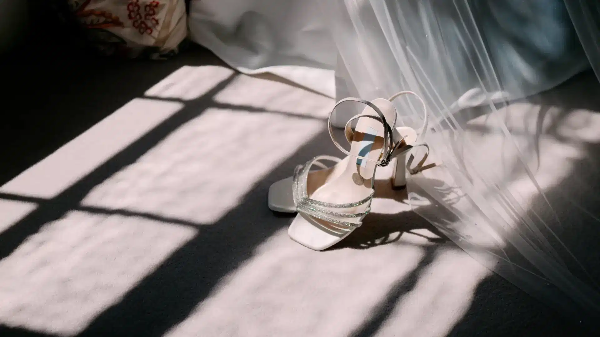 a pair of wedding shoes arranged on the carpet around the veil bathed in sunlight coming through the window