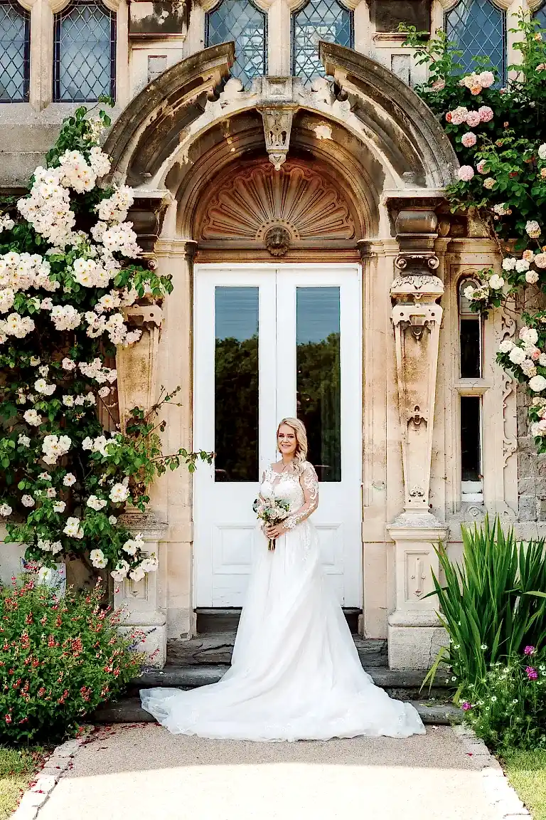 a woman in a wedding dress holding a bouquet in front of a door at Clevedon Hall