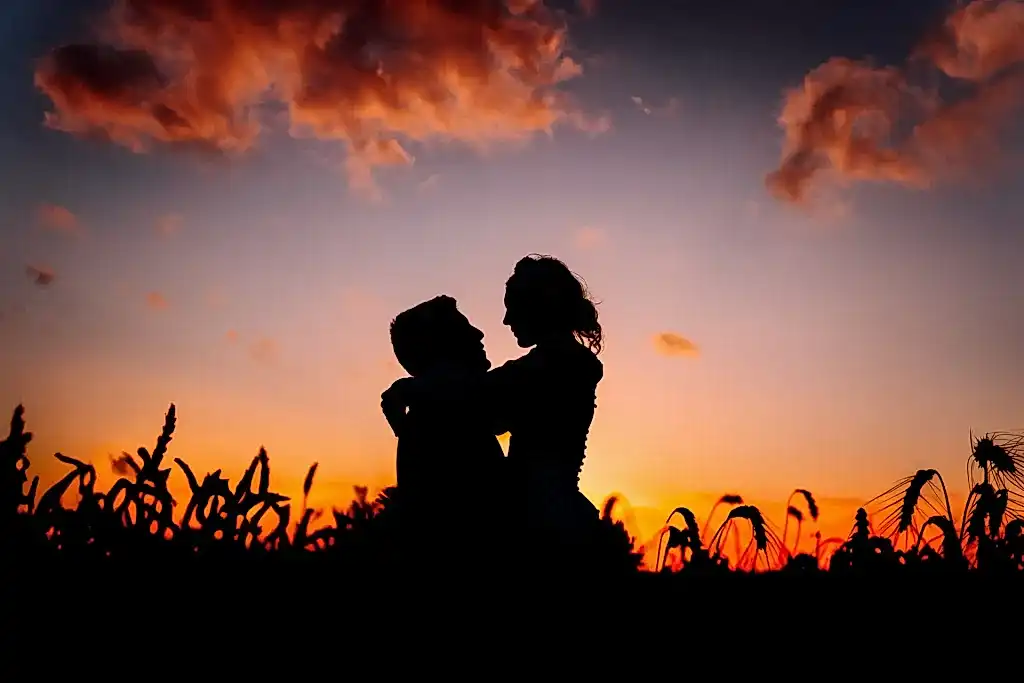couple-embrace-silhouette-corn-field-sunset a silhouette of a man and woman in an embrace in a field of corn at sunset