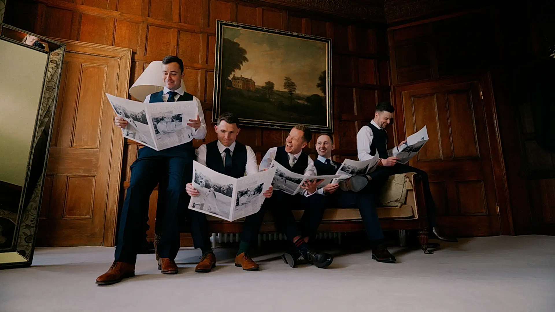 cotswolds wedding videographer captures the groomsmen reading the wedding day newspapers on the couch