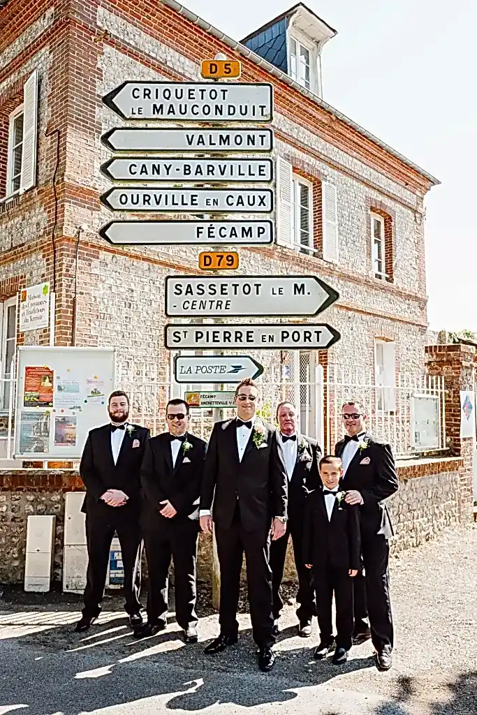 a group of groomsmen in black suits standing in front of a street sign in France on their wedding day