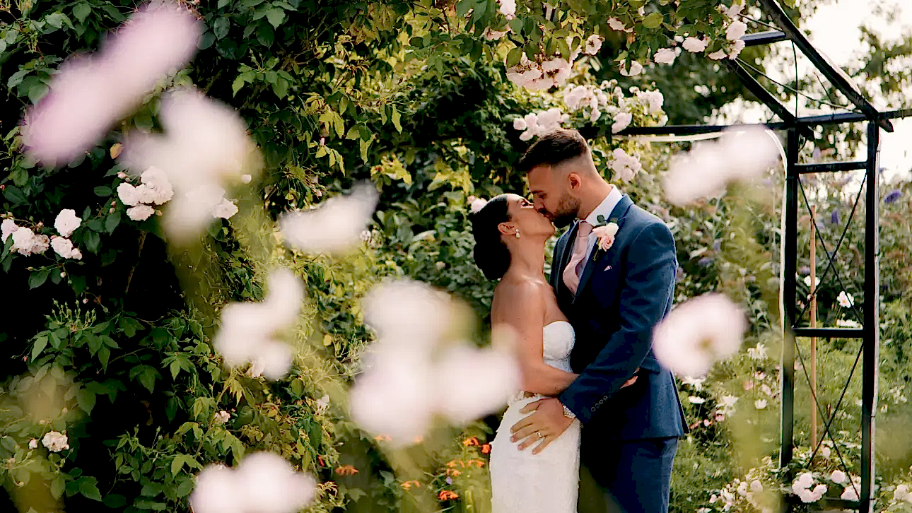 bride and groom kissing under roses at Kingscote Barn