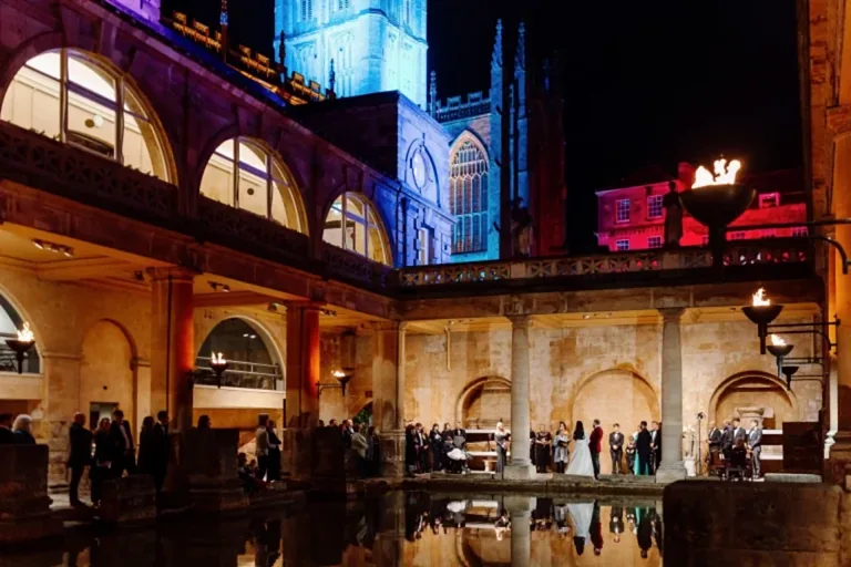 a wedding ceremony taking place around the baths at night time at the roman baths in somerset