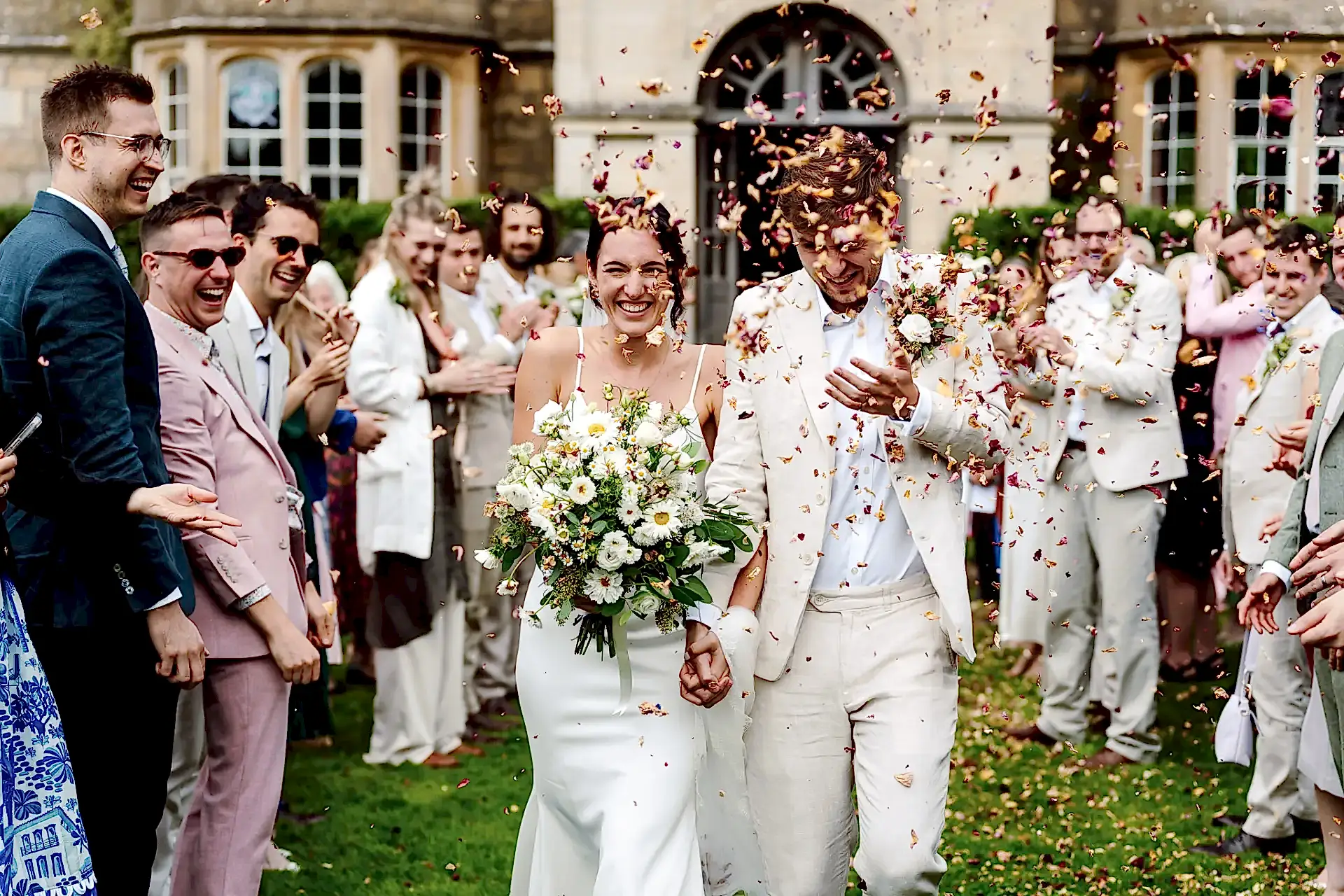 bride and groom walking through a shower of confetti at Hilles House in the Costwolds