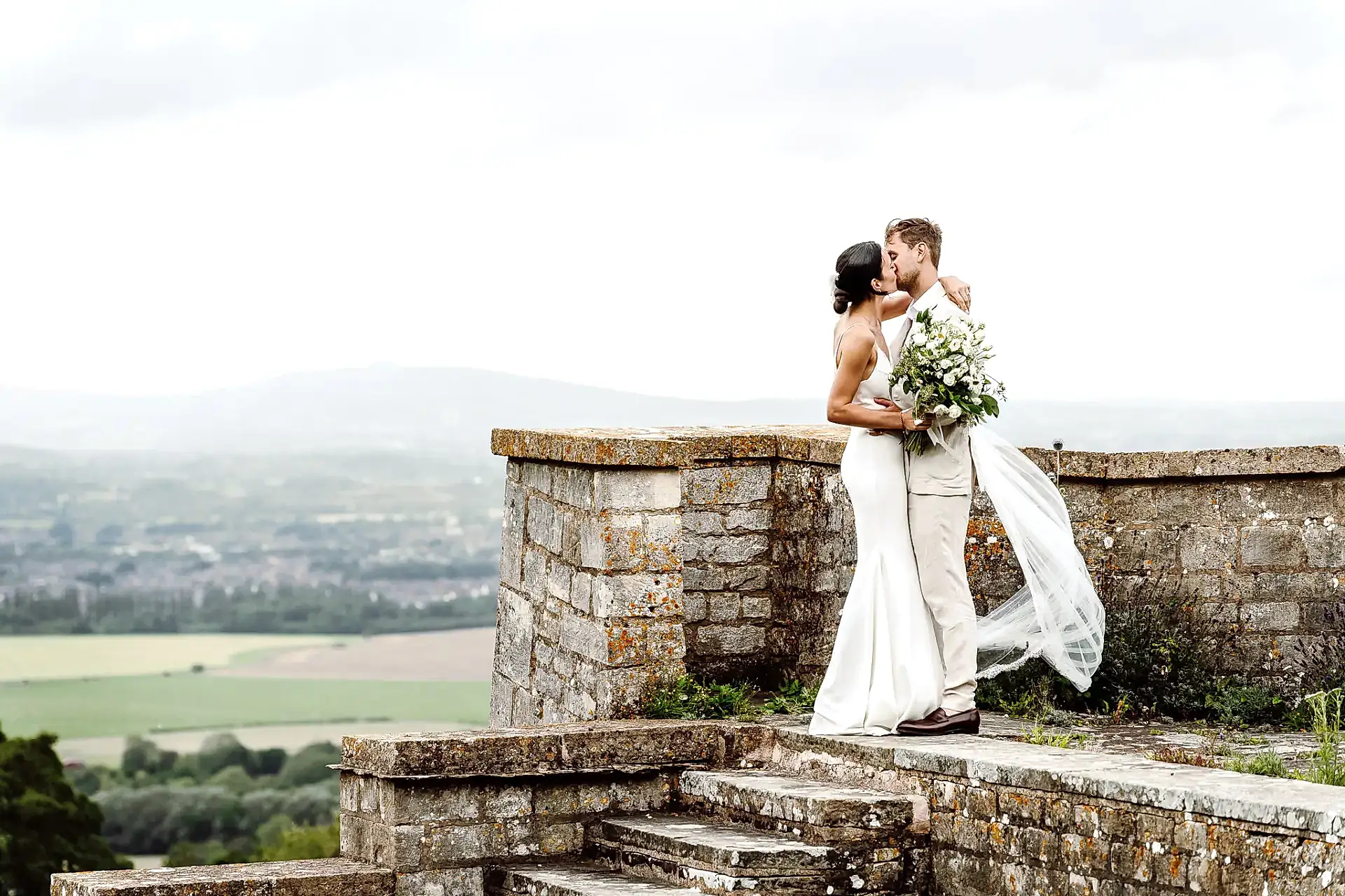 bride and groom kiss at with the view of the cotswolds landscape behind them on their wedding day